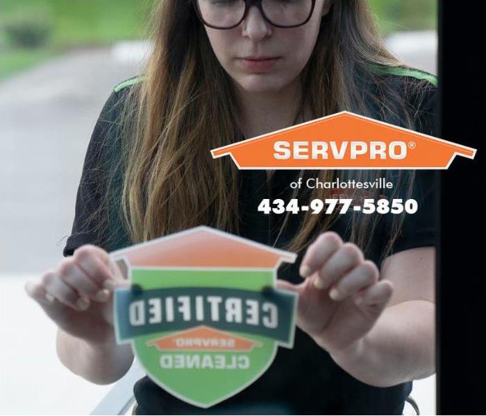 A SERVPRO of Charlottesville technician is placing a Certified: SERVPRO Cleaned sticker on the door to a commercial property 